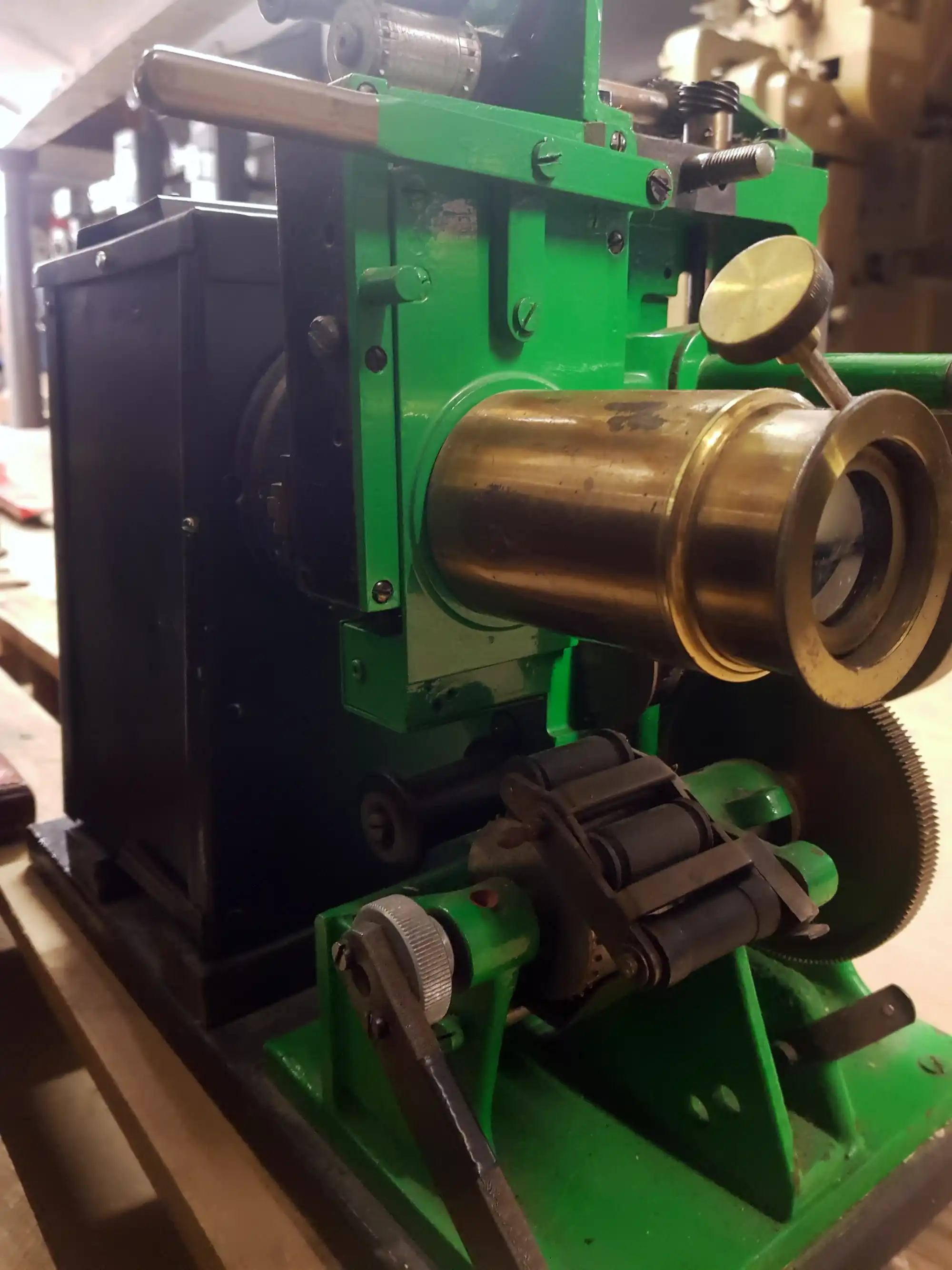 A black metal projector with green front and gold lens