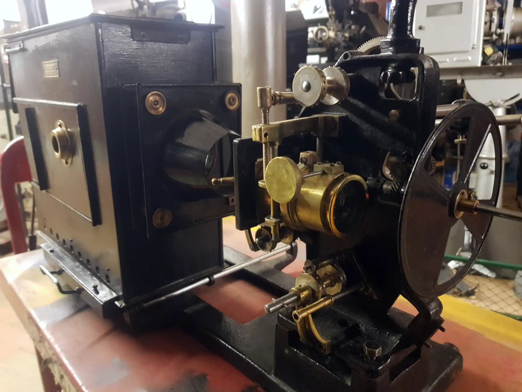 Black box lamphouse behind a black projector with gold lens and shutter at the front