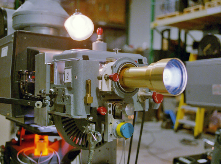 A grey film projector with gold lens