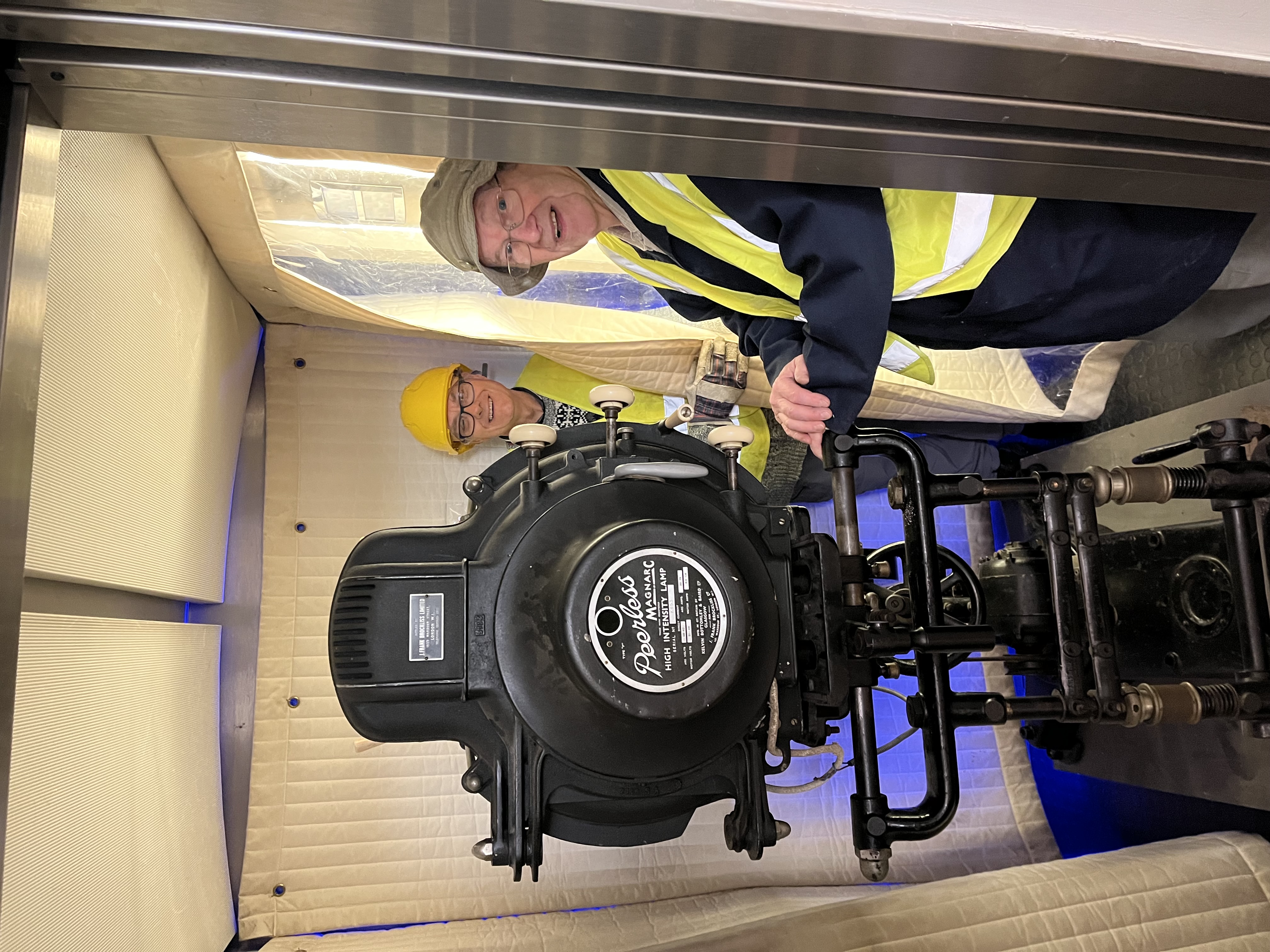 A cinema projector in a lift, held in place by two men.
