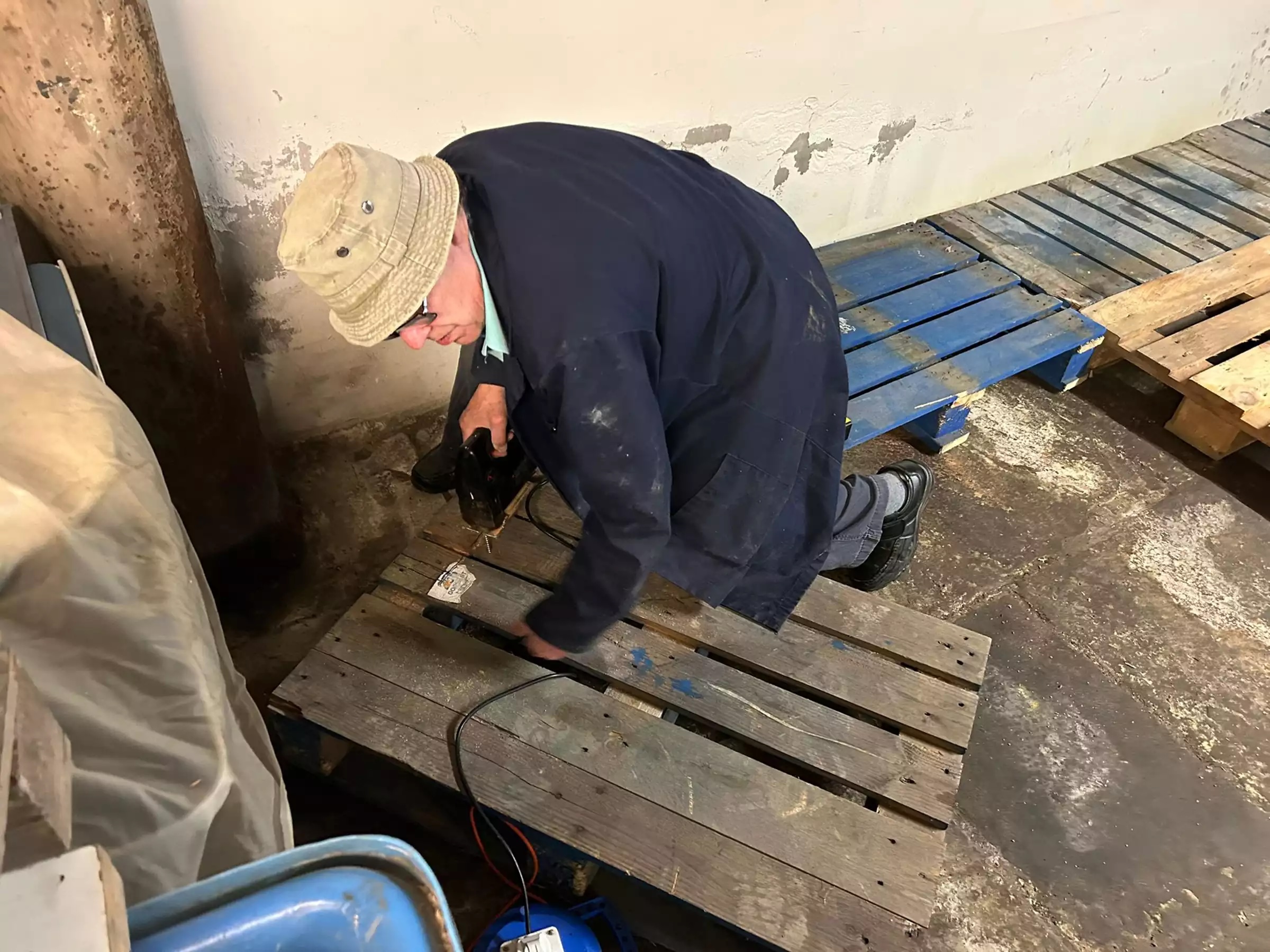 A man using a power tool on a wooden pallet on a hard floor