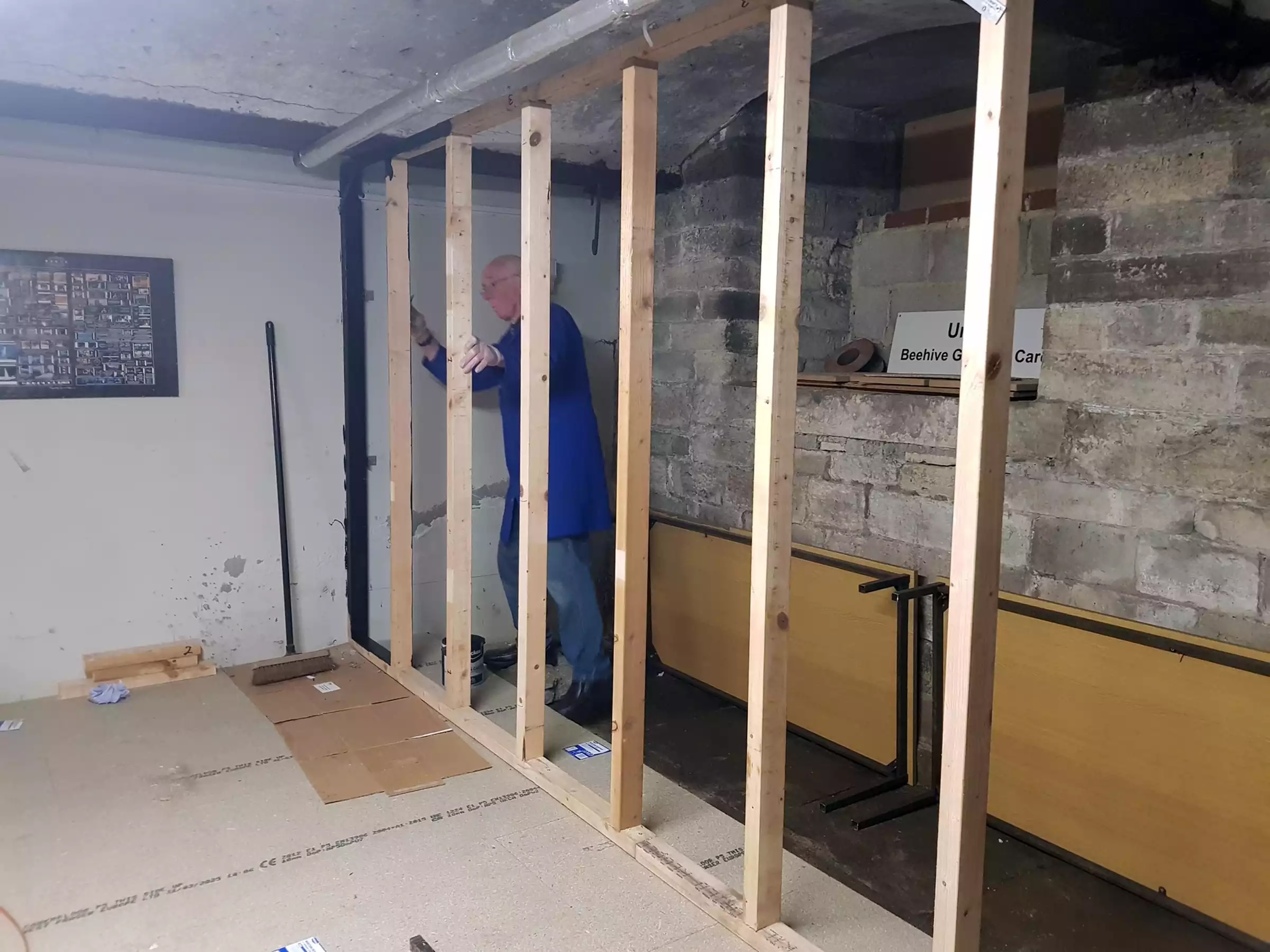 A man holding a constructed wooden stud wall vertical