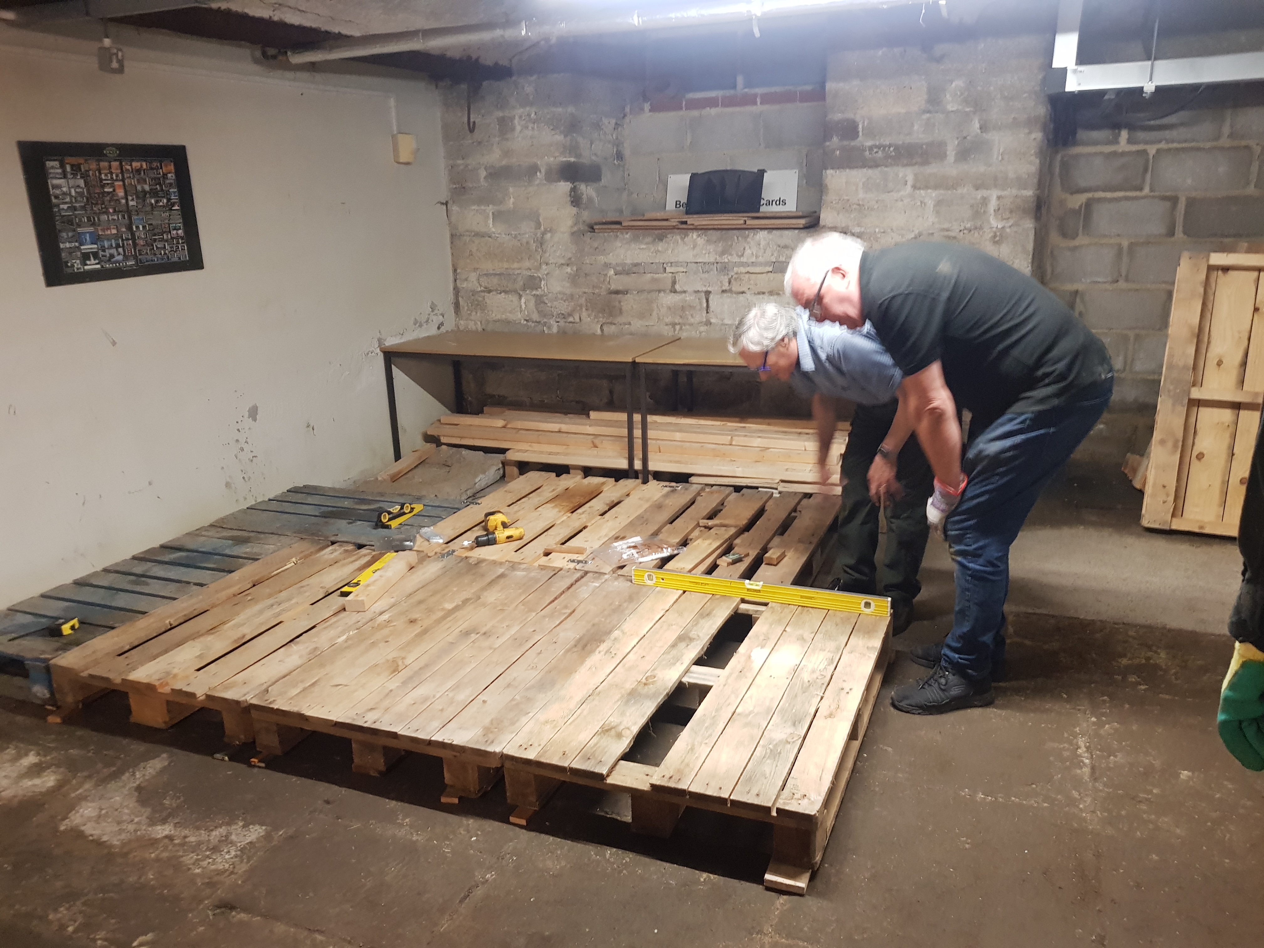 Two men standing over wooden pallets laid on the concrete floor