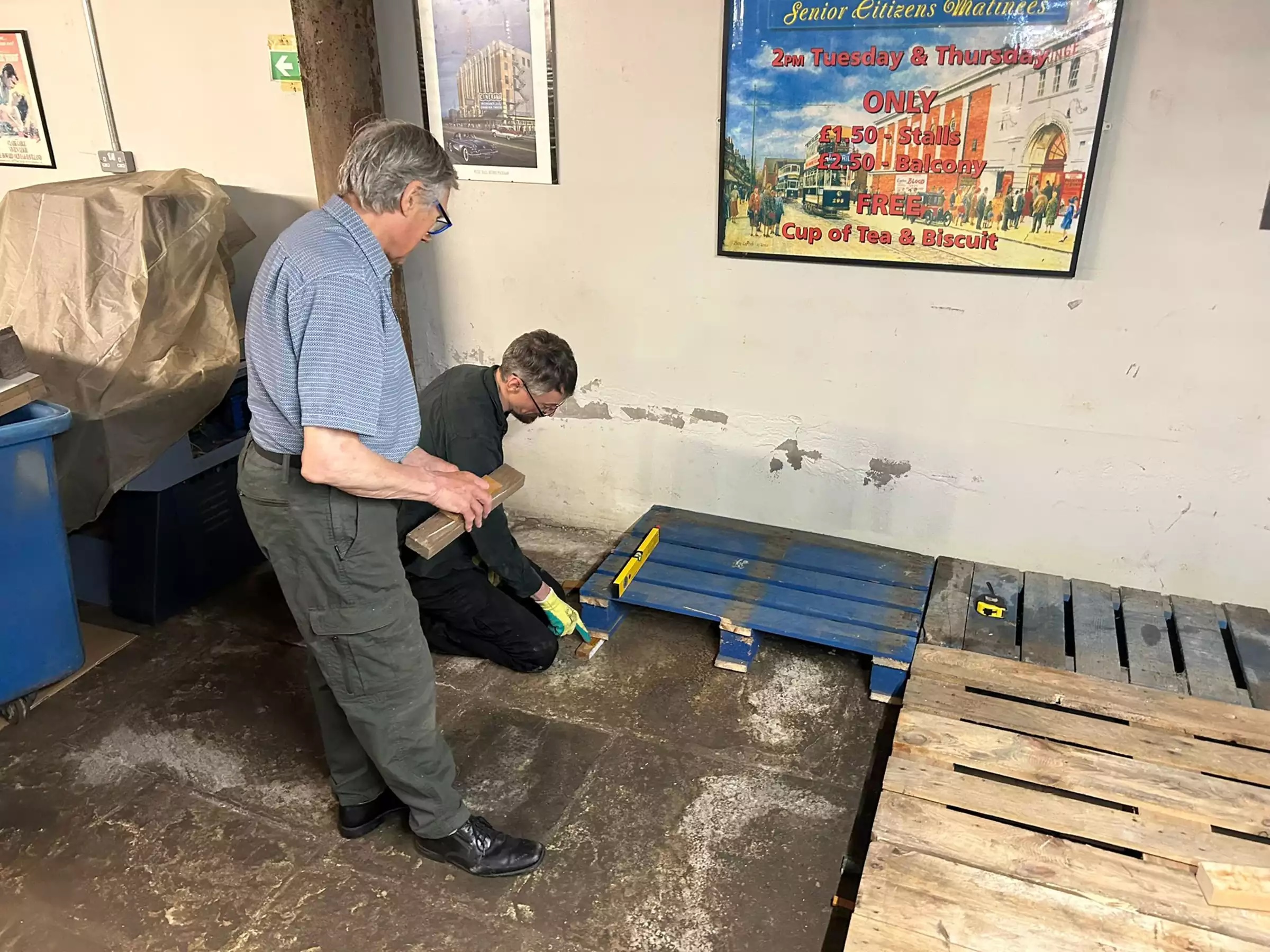 Two men laying wooden pallets on a hard floor