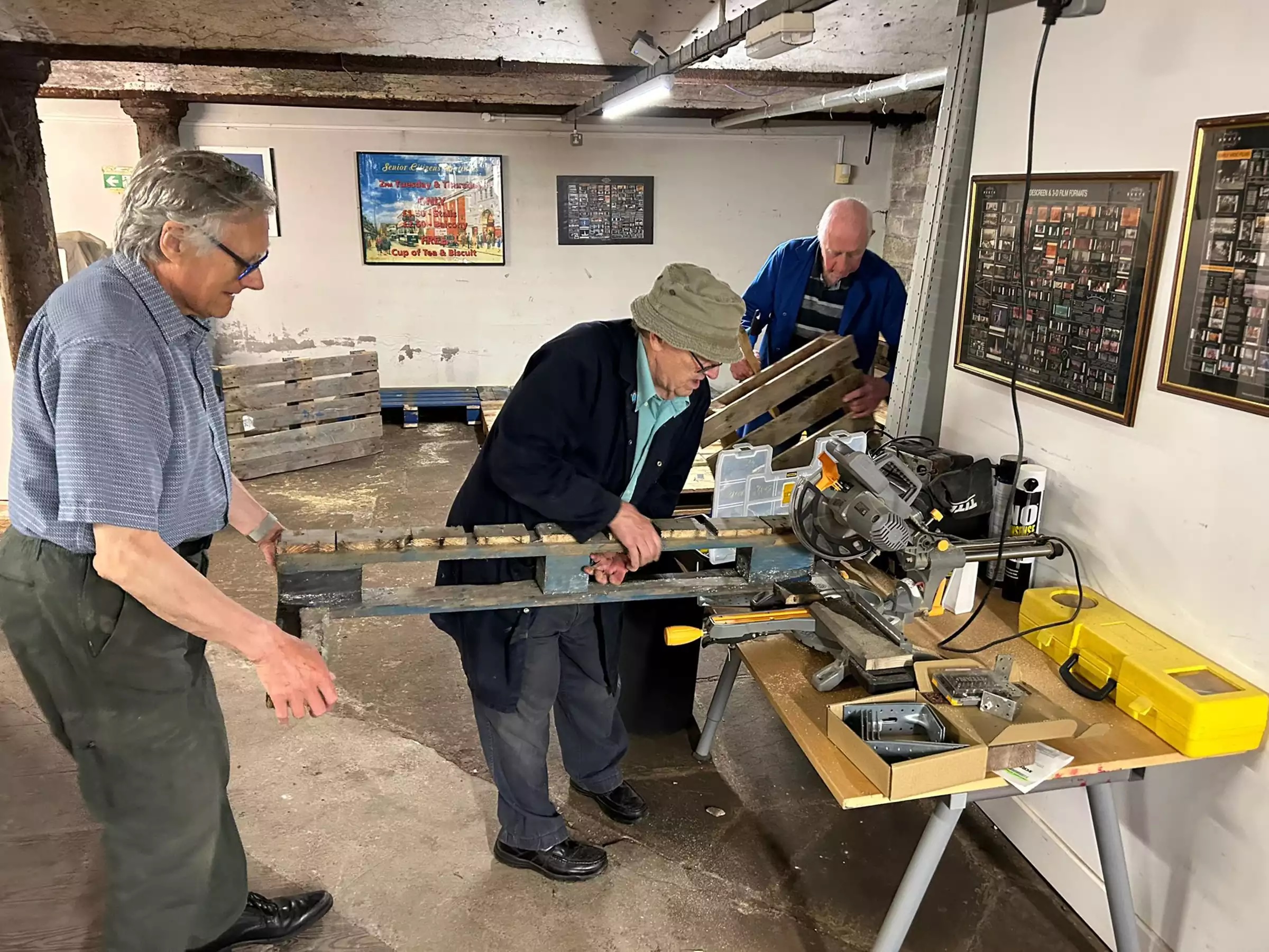 Three men cutting a wooden pallet to size for the floor