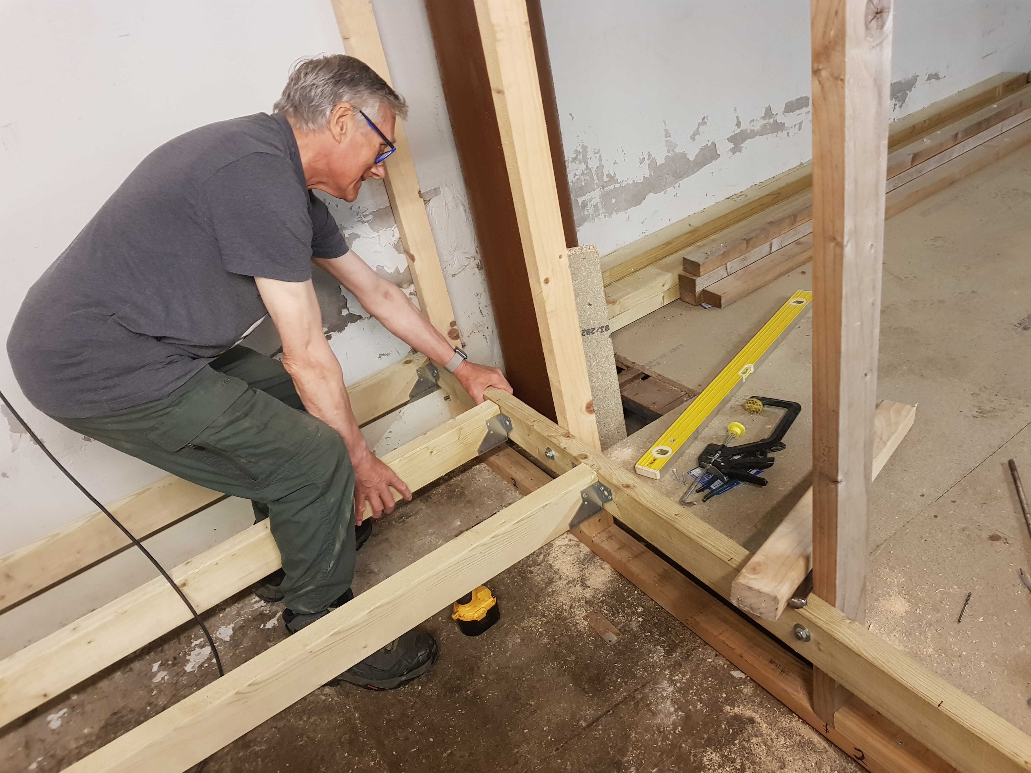 A man screwing on floor joists to a stud wall