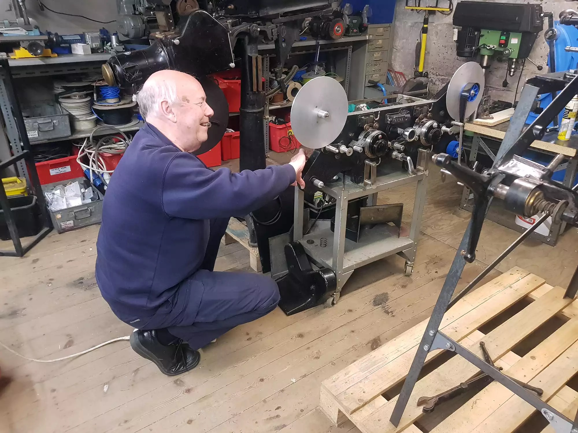 A man crouching beside a black film editing machine on a stand