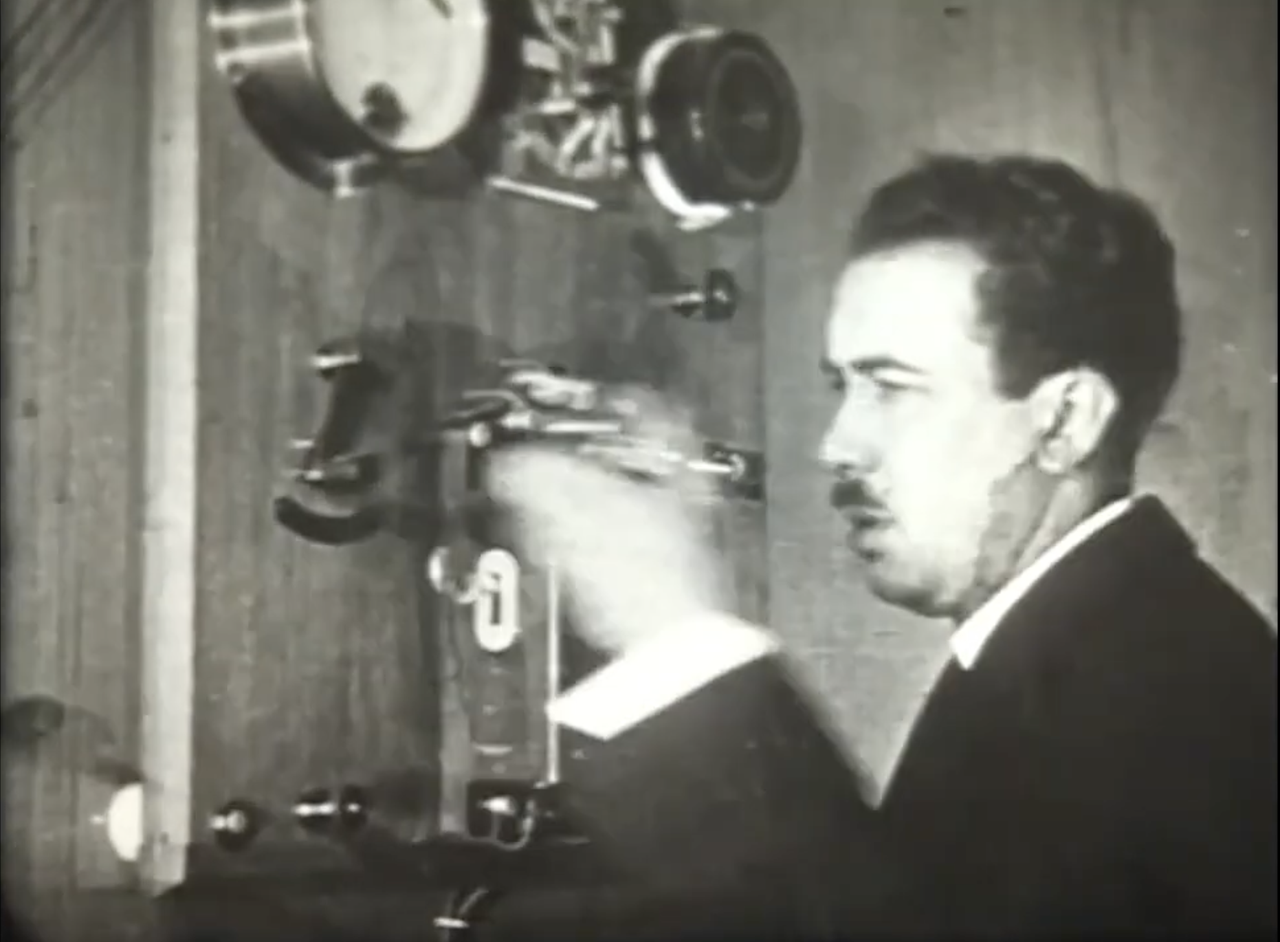 A black and white image of a man standing next to old telephony equipment